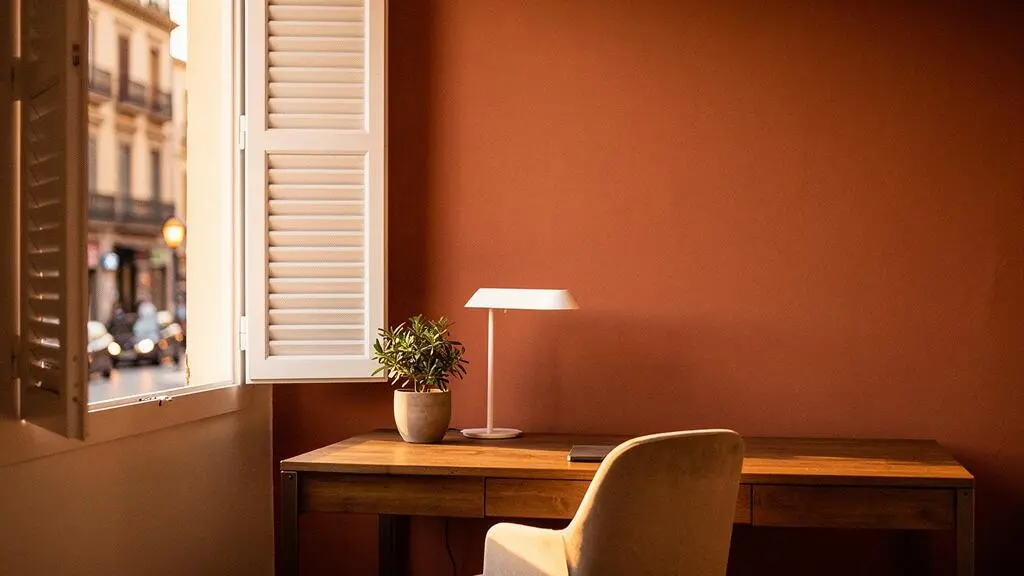 Espacio de home-office luminoso con luz natural cálida entrando por una ventana en un piso español, creando un ambiente de trabajo confortable para la vista