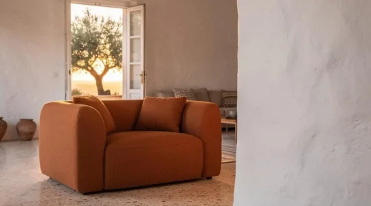 Salón español con un sofá de autor como punto focal, iluminado por luz natural mediterránea junto a una terraza