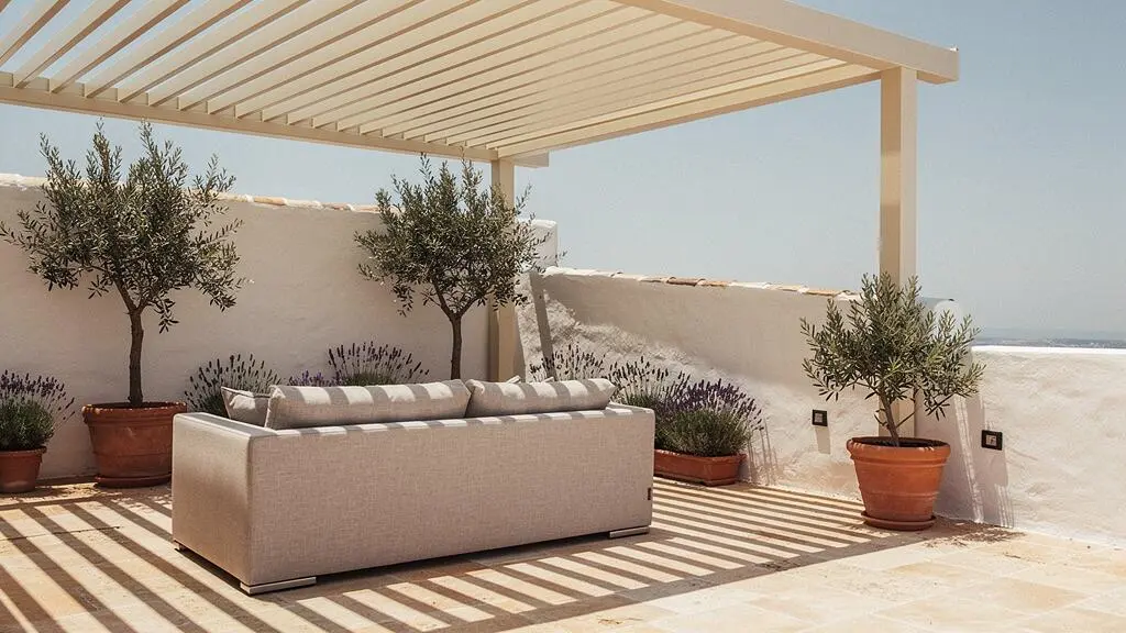 Terraza soleada española con pérgola bioclimática de aluminio blanco proyectando sombra fresca y luminosa sobre un salón exterior